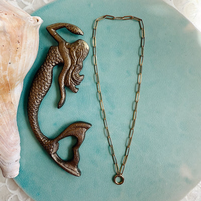 Gold paperclip-style charm chain necklace with elongated links, displayed on neutral background, perfect for layering or adding custom charms.